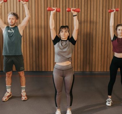 Three adults exercising with dumbbells in a gym setting, promoting fitness and healthy lifestyle.